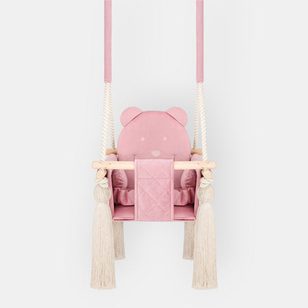 Altalena da interno per bambini in velluto Rosa, vista frontale con seduta trapuntata, barra in legno e nappe